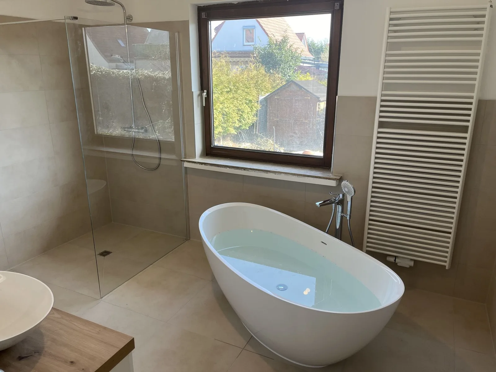Bad mit freistehender Wanne, bodengleicher Glasdusche, Handtuchheizkörper und Fenster zum Garten