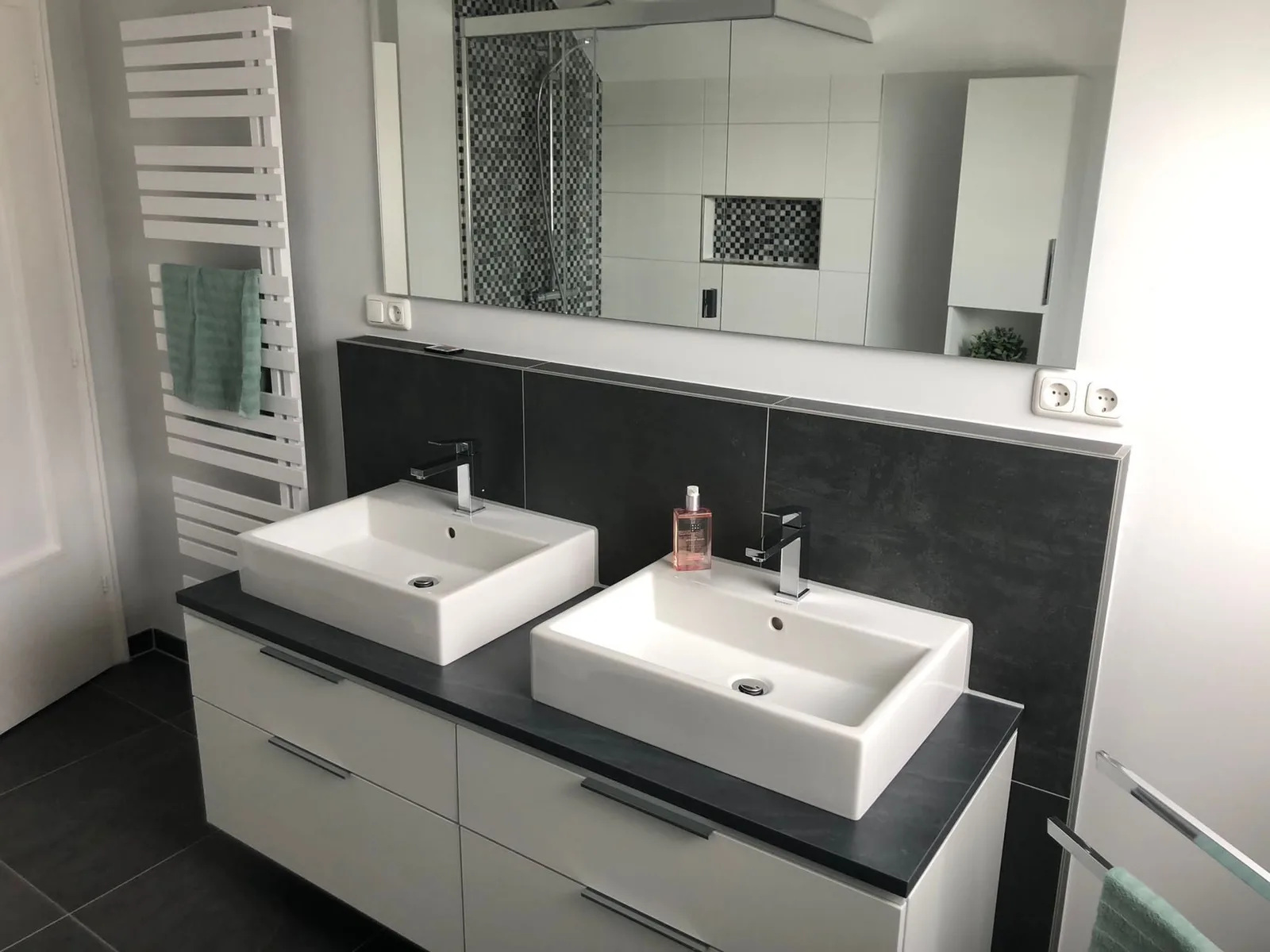 Doppelwaschtisch mit zwei eckigen Aufsatzbecken auf dunkler Platte, großer Spiegel und Designheizkörper