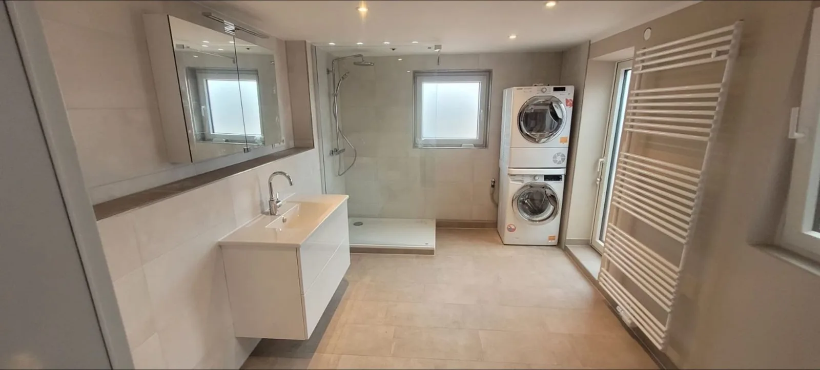Langes, helles Bad mit Waschtisch, Spiegelschrank, Walk-in-Dusche, Waschmaschine und Trockner